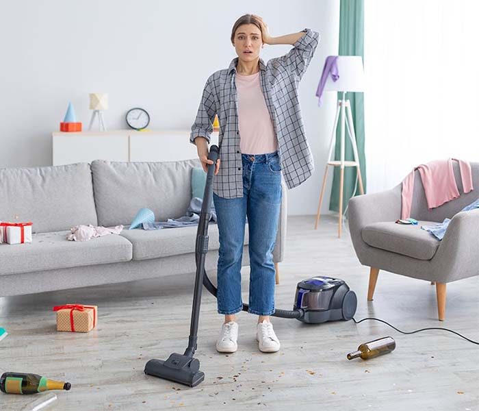 Frau in unaufgeräumter Wohnung mit Staubsauger in der Hand